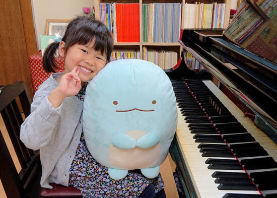 ピアノの前でぬいぐるみを抱いて笑う女の子の写真