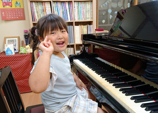 ピアノの前で満面の笑みでピースする女の子の写真